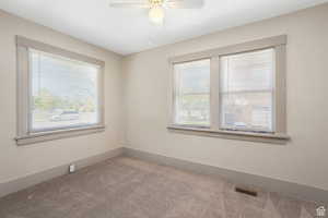 Spare room with a healthy amount of sunlight, a ceiling fan, carpet flooring, and visible vents