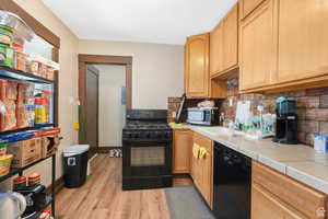 Kitchen with light brown cabinets, tile countertops, tasteful backsplash, light wood-style flooring, and black appliances