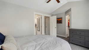 Bedroom featuring vaulted ceiling, carpet flooring, baseboards, ensuite bath, and ceiling fan