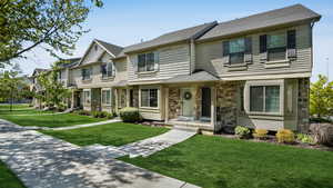 Multi unit property featuring stone siding, a front lawn, and a shingled roof