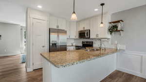 Kitchen with stainless steel appliances, a sink, a peninsula, light stone counters, and dark wood-style floors