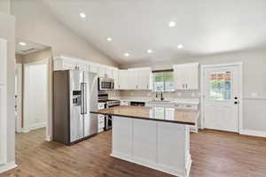 Kitchen with appliances with stainless steel finishes, a sink, white cabinetry, a kitchen island, and lofted ceiling
