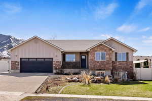 View of front of home featuring stone siding, a garage, concrete driveway, a mountain view, and a shingled roof