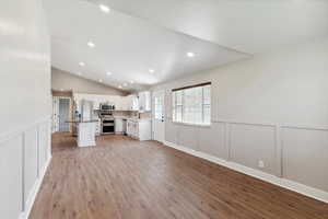 Unfurnished living room with a decorative wall, light wood finished floors, vaulted ceiling, recessed lighting, and wainscoting