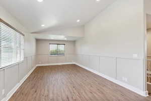 Empty room featuring vaulted ceiling, wood finished floors, recessed lighting, a decorative wall, and wainscoting