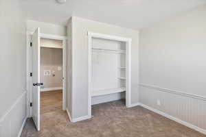 Unfurnished bedroom featuring carpet flooring, a closet, and a wainscoted wall