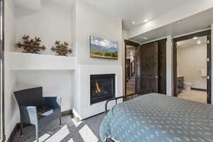 Carpeted bedroom featuring a glass covered fireplace, baseboards, a closet, ensuite bathroom, and recessed lighting