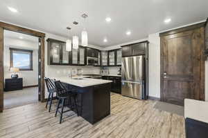 Kitchen with appliances with stainless steel finishes, glass insert cabinets, a peninsula, a sink, and baseboards