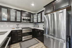 Kitchen with high quality appliances, light countertops, tasteful backsplash, light wood-type flooring, and glass insert cabinets