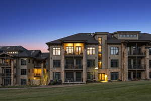 Back of property at dusk with board and batten siding, a lawn, and a balcony