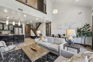 Living area featuring light wood-type flooring, high vaulted ceiling, stairs, recessed lighting, and baseboards