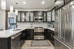 Kitchen featuring premium appliances, a sink, a peninsula, light countertops, and hanging light fixtures