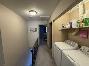 Clothes washing area with washer and dryer, light carpet, a textured ceiling, and attic access