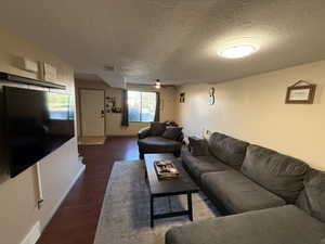 Living area featuring a textured ceiling, wood finished floors, a ceiling fan, and baseboards