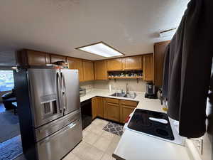 Kitchen with stainless steel refrigerator with ice dispenser, a sink, black dishwasher, open shelves, and brown cabinetry