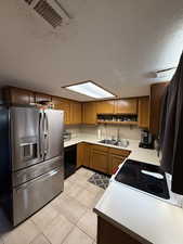 Kitchen featuring stainless steel refrigerator with ice dispenser, a sink, a textured ceiling, black dishwasher, and brown cabinetry