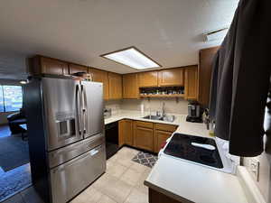 Kitchen featuring stainless steel fridge, a sink, black dishwasher, brown cabinets, and a textured ceiling