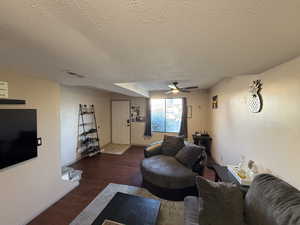 Living room with a textured ceiling, wood finished floors, ceiling fan, and baseboards