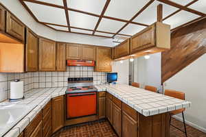 Kitchen featuring range with electric cooktop, tile counters, under cabinet range hood, and a peninsula
