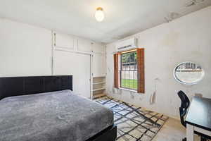 Bedroom featuring an AC wall unit, light carpet, and baseboards