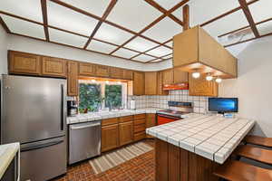 Kitchen with appliances with stainless steel finishes, a sink, under cabinet range hood, decorative backsplash, and a peninsula