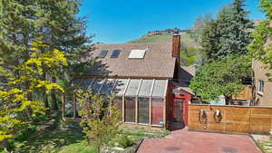 Back of property featuring roof with shingles, a chimney, a greenhouse, and an outbuilding