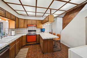 Kitchen with tile counters, stainless steel dishwasher, range with electric stovetop, a peninsula, and under cabinet range hood