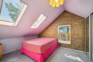 Bedroom featuring vaulted ceiling, a skylight, carpet, brick wall, and baseboards