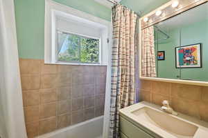 Bathroom with shower / bath combination with curtain, vanity, and tile walls