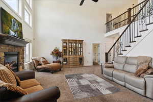 Carpeted living area featuring a high ceiling, plenty of natural light, a ceiling fan, a fireplace, and stairway