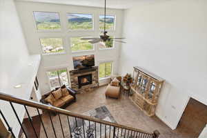 Living area featuring a ceiling fan, a high ceiling, carpet floors, a stone fireplace, and stairs