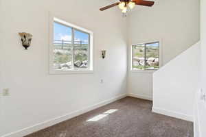 Carpeted spare room featuring ceiling fan and baseboards