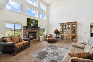 Living area with a high ceiling, carpet floors, and a stone fireplace
