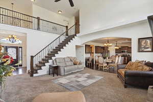 Carpeted living area with a chandelier, a high ceiling, arched walkways, stairs, and ceiling fan