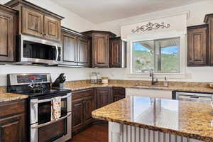 Kitchen featuring appliances with stainless steel finishes, a sink, dark brown cabinetry, and light stone countertops