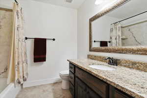 Bathroom with toilet, baseboards, tile patterned floors, vanity, and shower / tub combo