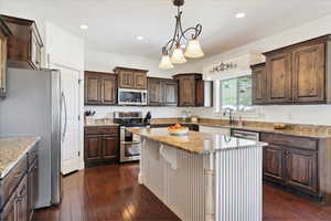 Kitchen featuring appliances with stainless steel finishes, a center island, dark brown cabinets, dark wood-style floors, and a sink