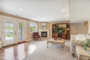 Living area featuring recessed lighting, a premium fireplace, wood finished floors, french doors, and baseboards