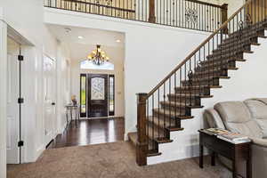 Foyer with a high ceiling, carpet flooring, a chandelier, stairs, and baseboards