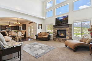 Carpeted living area featuring arched walkways, a stone fireplace, a chandelier, and a towering ceiling
