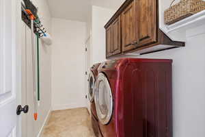 Clothes washing area with separate washer and dryer, cabinet space, and baseboards