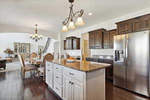 Kitchen featuring stainless steel refrigerator with ice dispenser, a center island, arched walkways, dark brown cabinetry, and dark wood-style floors
