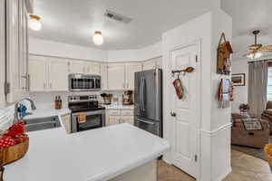 Kitchen with stainless steel appliances, a sink, ceiling fan, light tile patterned floors, and light countertops