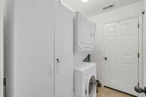 Washroom with stacked washing machine and dryer and light tile patterned floors