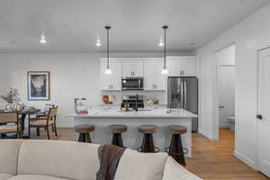 Kitchen featuring appliances with stainless steel finishes, light wood-type flooring, a sink, baseboards, and white cabinets
