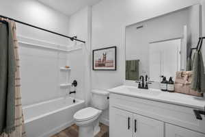 Full bathroom with wood finished floors, toilet, shower / bath combo with shower curtain, vanity, and baseboards