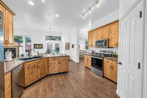 Kitchen featuring stainless steel appliances, a sink, a peninsula, dark wood-style floors, and dark stone counters