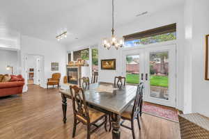 Dining space with a tiled fireplace, a chandelier, wood finished floors, and french doors