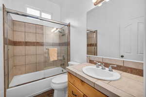 Bathroom with toilet, vanity, and combined bath / shower with glass door
