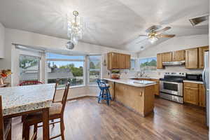 Kitchen featuring stainless steel appliances, a peninsula, brown cabinets, under cabinet range hood, and vaulted ceiling